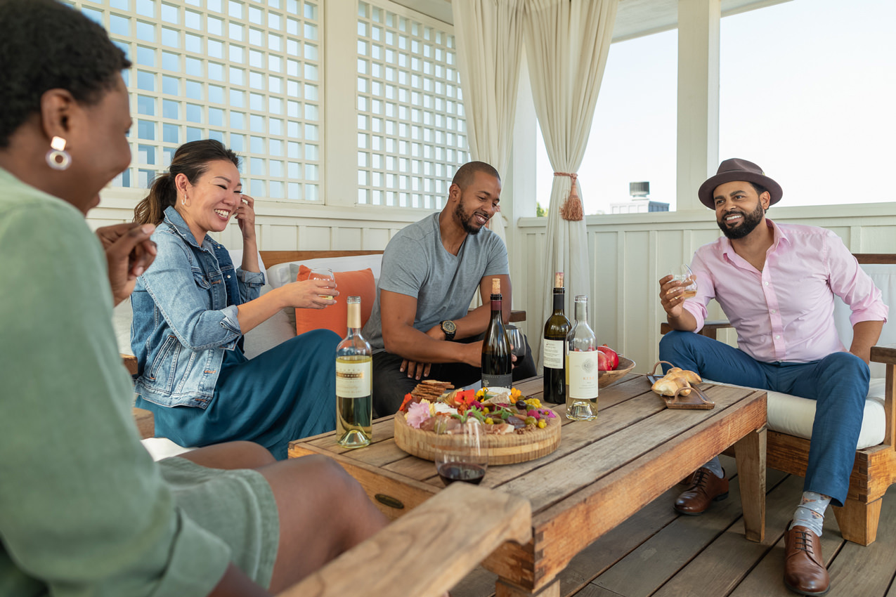group of four friends laughing and drinking wine on an outdoor porch