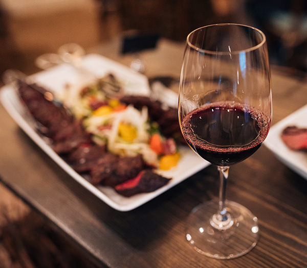 glass of red wine with platter of food in background