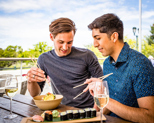 two men sitting outside eat sushi paired with white wine