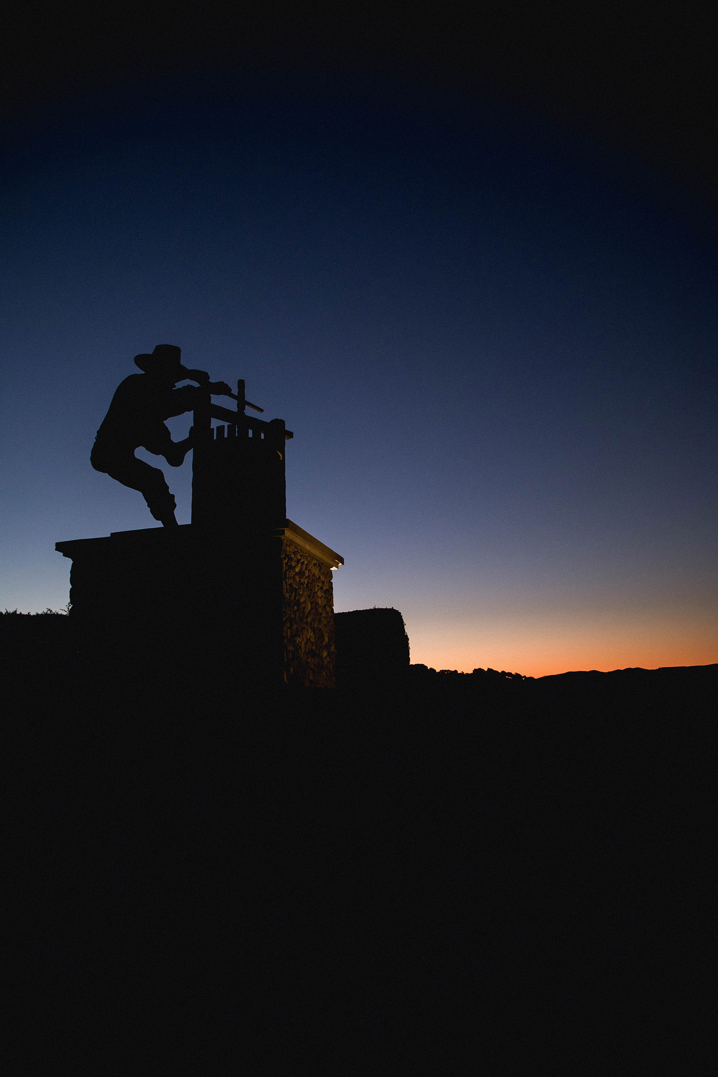 large statue of wine press worker silhouetted against sky and hills at dusk
