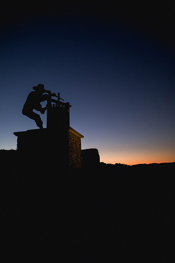 large statue of wine press worker silhouetted against sky and hills at dusk