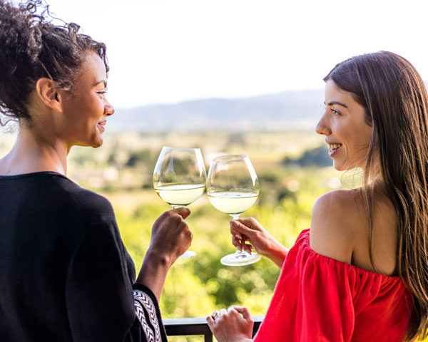 two women toast with white wine from a balcony overlooking Napa Valley