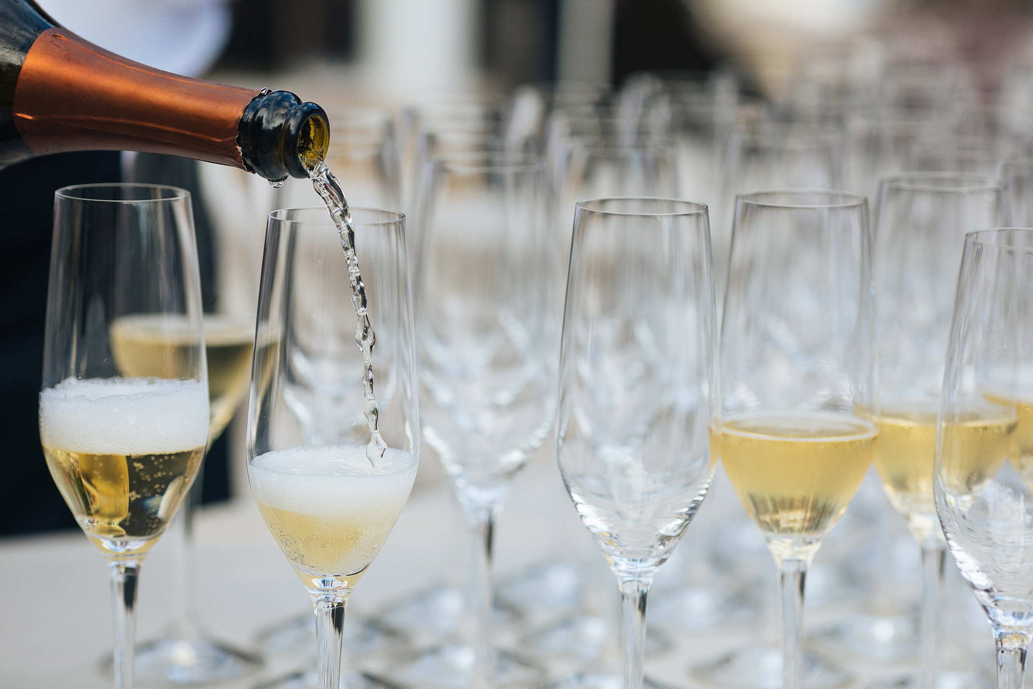 sparkling wine pouring from bottle into large grouping of champagne flutes on a table