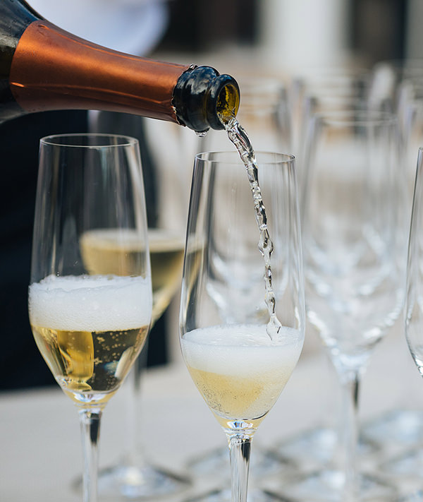 sparkling wine pouring from bottle into large grouping of champagne flutes on a table