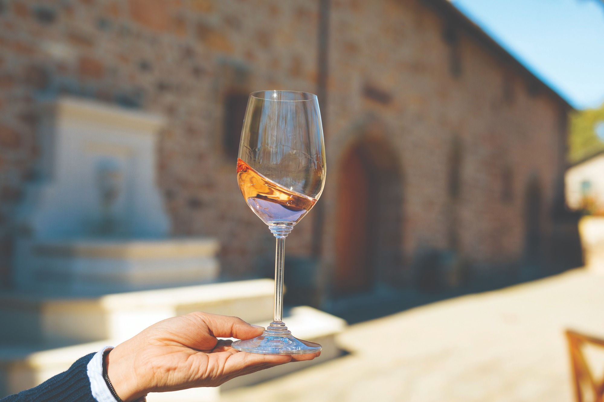 a hand holding a glass of rosé wine in front of a rock building